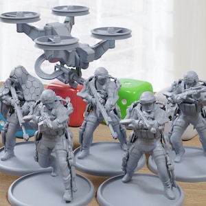 Op de afbeelding: Een set van grijze plastic miniatuurfiguurtjes van soldaten, elk met een wapen in de hand, staand op ronde bases. Een grijze plastic drone met vier propellers zweeft boven de figuurtjes.