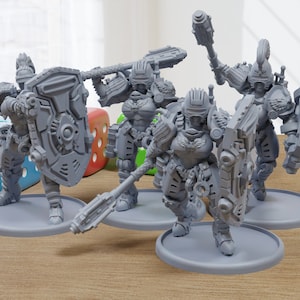 Puede incluir: Cuatro figuras en miniatura de plástico gris de guerreros que llevan armadura y sostienen armas. Las figuras están de pie sobre bases redondas.