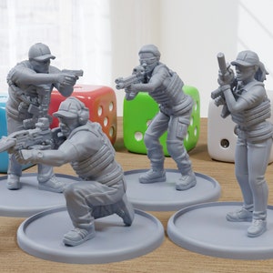 May include: Four gray plastic figurines of people wearing tactical gear and holding guns. The figurines are standing on gray circular bases. The figurines are on a wooden surface with three colorful dice.