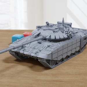 Könnte beinhalten: Ein graues Modell eines T-72-Panzers mit einem langen Lauf und einem Turm mit einer großen, flachen Oberseite. Der Panzer steht auf einer Holzoberfläche.