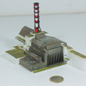 Pode incluir: Um modelo detalhado de uma usina nuclear com uma chaminé alta de listras vermelhas e brancas. O modelo é feito de plástico cinza e branco e está sentado em uma superfície branca.