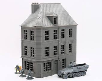 Puede incluir: Un modelo de plástico gris de un edificio de tres pisos con una fachada detallada, que incluye ventanas, puertas y un techo. El edificio está sobre un fondo blanco. Un modelo de plástico gris de un vehículo militar está en primer plano.