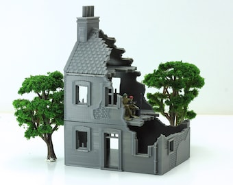 May include: A gray, two-story, ruined building with a chimney and a missing roof. Two miniature figures are standing on the second floor. There are two green trees on either side of the building.
