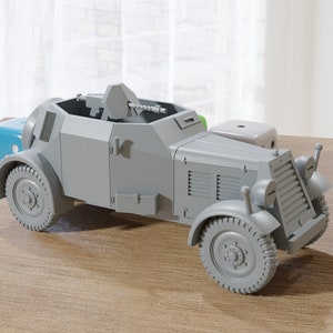 May include: A grey model of a German Sd.Kfz. 234/2 armoured car with a machine gun mounted on top. The model is on a wooden surface.