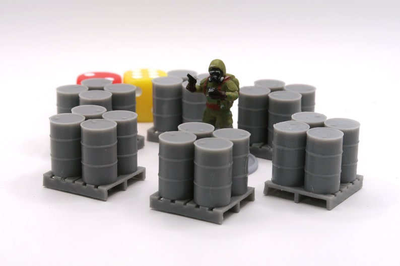 May include: Three sets of gray plastic barrels on pallets. Each set has four barrels stacked on top of each other. A miniature figure of a person wearing a gas mask and camouflage clothing stands in front of the barrels.