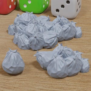 以下が含まれることがあります： 木製の表面に、灰色のプラスチック製のゴミ袋の山が置かれています。背景には、カラフルなサイコロが4つあります。