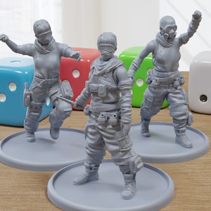 Könnte beinhalten: Drei graue Plastik-Miniaturfiguren von Personen in futuristischer Kleidung und Accessoires. Die Figuren stehen auf runden Sockeln. Die Figuren sind in Action-Posen dargestellt.