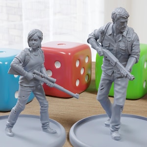 Puede incluir: Dos figuras pintadas de gris de personajes de un videojuego. El personaje femenino sostiene un rifle y el personaje masculino sostiene una escopeta. Las figuras están de pie sobre bases grises.