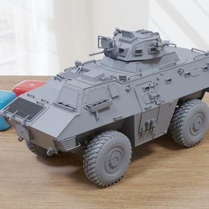May include: A grey model of an armoured vehicle, featuring a turret, wheels, and detailed exterior elements. The model is displayed on a wooden surface, with blue and red dice nearby.
