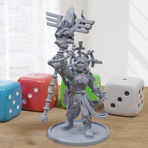 May include: A gray miniature figurine of a character holding a staff, standing on a round base. The figurine is surrounded by four large dice in blue, red, green, and white. The dice are on a wooden surface.