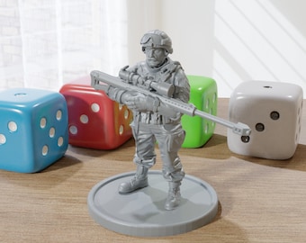 May include: A gray plastic miniature figurine of a soldier holding a rifle. The soldier is wearing a helmet and camouflage clothing. The figurine is standing on a gray plastic base. There are three dice in the background, one blue, one red, and one gray.