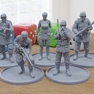 Puede incluir: Seis figuras en miniatura de plástico gris de soldados, cada una de pie sobre una base de plástico gris. Las figuras llevan uniformes militares y sostienen armas. Las figuras están dispuestas en semicírculo sobre una superficie de madera.