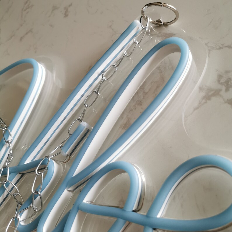 May include: A blue neon sign with a white outline and a chain hanging from the top. The sign is made of clear acrylic and has a silver chain.