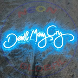 May include: A bright blue neon sign featuring the text "Devil May Cry" in a flowing, cursive script font. The sign emits a vibrant glow, illuminating the surrounding area with a cool blue light, and is mounted on a clear, transparent backing.