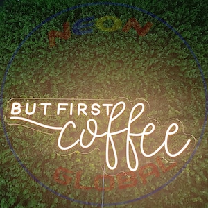 May include: White neon sign with the text "But first, coffee" in a cursive font. The sign is mounted on a green wall.