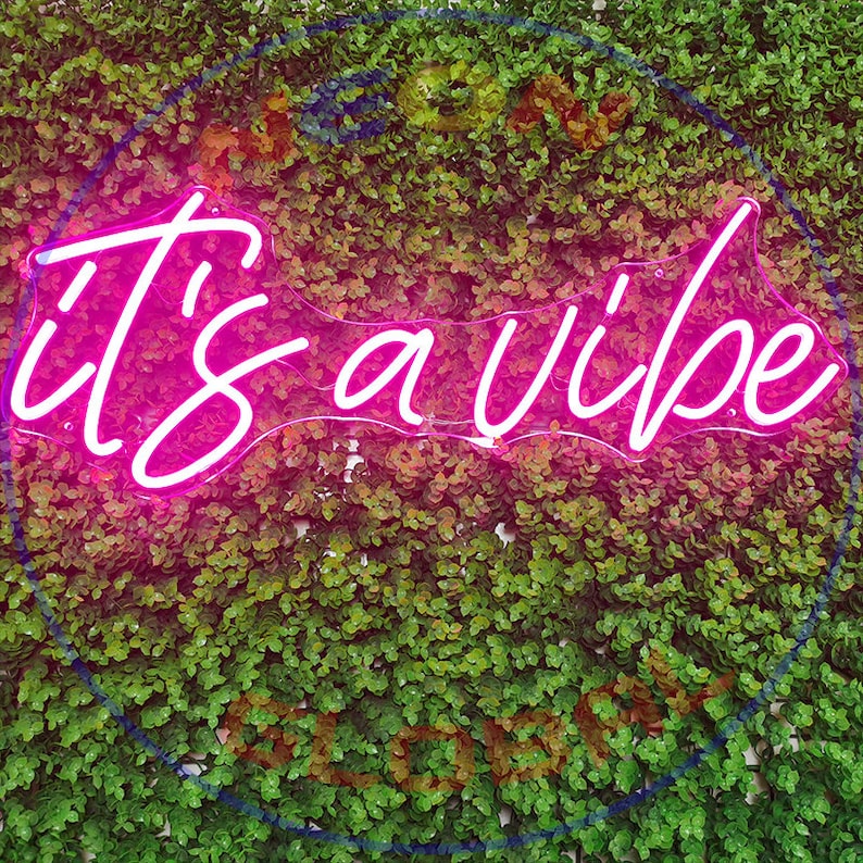 May include: Pink neon sign with the text "it's a vibe" on a green leafy background.