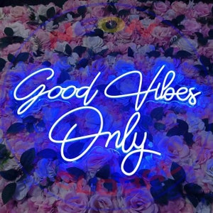 May include: White neon sign with blue glow, against a background of pink and purple flowers. The sign reads "Good Vibes Only".