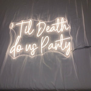 Op de afbeelding: Een wit neonbord met de tekst "Til Death do us Party" op een witte achtergrond.