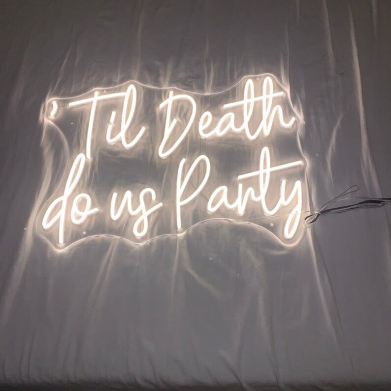 Op de afbeelding: Een wit neonbord met de tekst "Til Death do us Party" op een witte achtergrond.