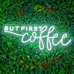 May include: White neon sign with the text "BUT FIRST COFFEE" in a cursive font. The sign is on a green background.