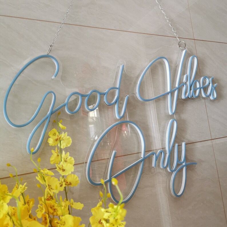 May include: A blue neon sign with the text "Good Vibes Only" hanging on a white tiled wall. The sign is made of clear acrylic and has a white backing.