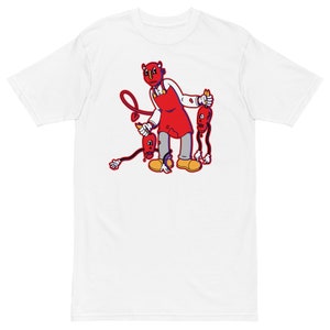 May include: White t-shirt with a cartoon illustration of a red devil character holding two red figures with devil horns and tails. The devil character is wearing a red apron and has a red heart-shaped tail.
