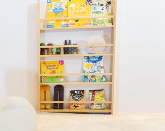 May include: A wooden bookshelf with five shelves, filled with colorful children's books and toys. The bookshelf is light brown and has a simple design.