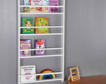May include: White wooden bookshelf with six shelves, mounted on a gray wall. The shelves are filled with colorful children's books. A rainbow wooden toy and an abacus are on a wooden table in the corner.