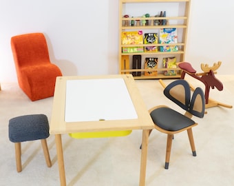 May include: A wooden children's table with a white top and a yellow storage compartment. The table is surrounded by a grey stool, a grey chair with bunny ears, and a rocking moose toy.