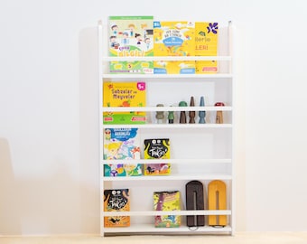 May include: White bookshelf with five shelves, filled with colorful children's books. The books have titles in Turkish. The top shelf has a book titled "Ilerie Leri". The second shelf has a book titled "Sebzeler ve Meyveler". The third shelf has a book titled "Sekillerin Degisinligi". The fourth shelf has a book titled "Tango". The bottom shelf has a book titled "Tango".