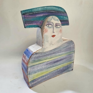 May include: A ceramic sculpture of a person with a striped hat and shirt. The sculpture is painted in shades of blue, purple, green, and white.