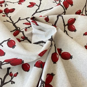 Könnte beinhalten: Nahaufnahme eines beigefarbenen Stoffes mit einem sich wiederholenden Muster aus roten Beeren und braunen Zweigen. Der Stoff ist so gefaltet, dass das Muster aus verschiedenen Blickwinkeln sichtbar ist.