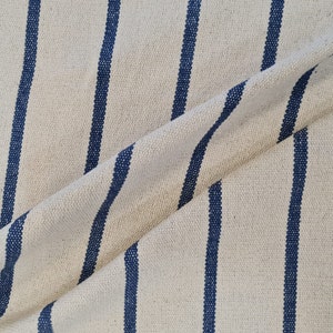 May include: Close-up of a white fabric with blue stripes. The fabric is woven and has a textured surface.