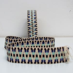 May include: A close-up of a beige, blue, and black patterned ribbon. The ribbon is woven with a geometric design.