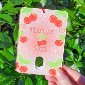 May include: A pink and white glass ornament with a cherry pattern and the text "I love you much".