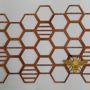 Puede incluir: Un dise&ntilde;o de panal de abeja de madera con un recorte de abeja amarilla. El panal est&aacute; hecho de formas hexagonales individuales, cada una con un peque&ntilde;o agujero en el centro. La abeja est&aacute; colocada en el centro del panal, con las alas extendidas.