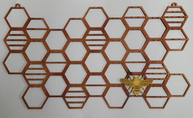 Puede incluir: Un dise&ntilde;o de panal de abeja de madera con un recorte de abeja amarilla. El panal est&aacute; hecho de formas hexagonales individuales, cada una con un peque&ntilde;o agujero en el centro. La abeja est&aacute; colocada en el centro del panal, con las alas extendidas.