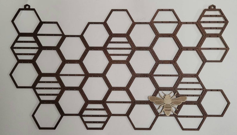 Puede incluir: Un soporte para pendientes de madera en forma de panal con un peque&ntilde;o recorte de abeja de madera. El soporte tiene 18 compartimentos hexagonales para pendientes.