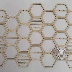 Puede incluir: Organizador de pared de madera en forma de panal con un recorte de abeja blanca. El organizador tiene 20 compartimentos hexagonales.