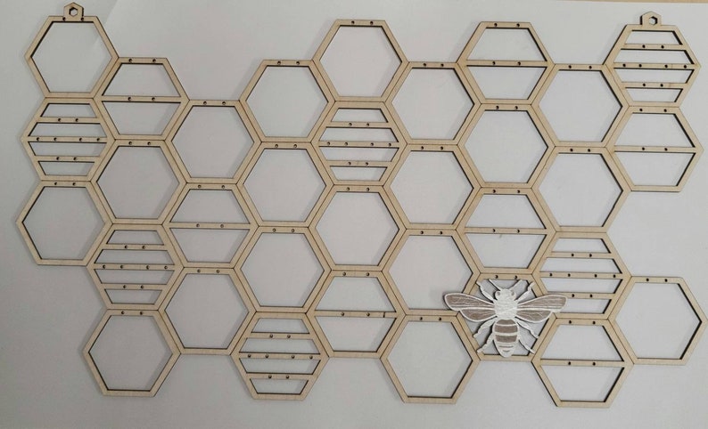 Puede incluir: Organizador de pared de madera en forma de panal con un recorte de abeja blanca. El organizador tiene 20 compartimentos hexagonales.