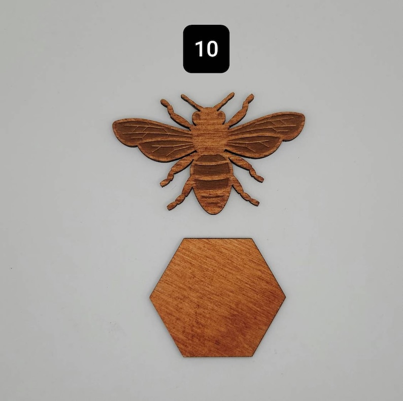 Puede incluir: Un recorte de abeja de madera con un dise&ntilde;o de panal. La abeja es marr&oacute;n y tiene alas detalladas. El panal tambi&eacute;n es marr&oacute;n y tiene una forma hexagonal.