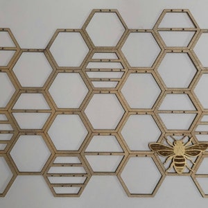 Puede incluir: Un organizador de pared de madera en forma de panal con un recorte de abeja dorada. El organizador tiene 20 compartimentos hexagonales y es perfecto para exhibir objetos peque&ntilde;os.