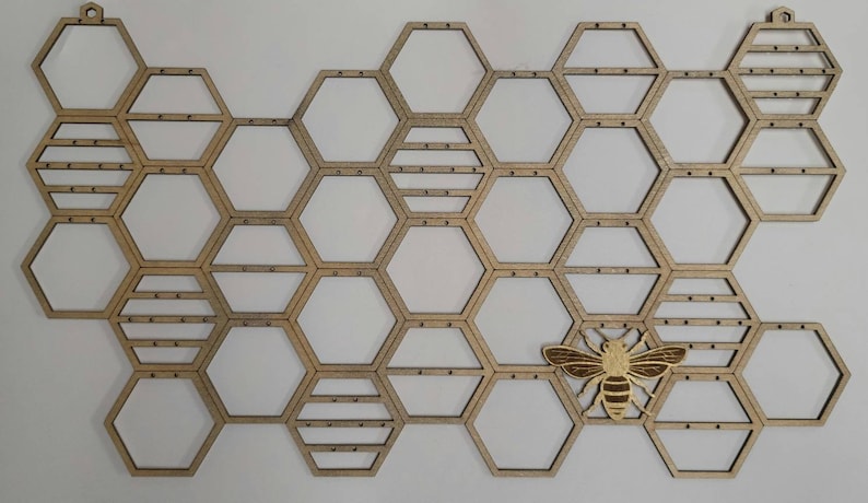Puede incluir: Un organizador de pared de madera en forma de panal con un recorte de abeja dorada. El organizador tiene 20 compartimentos hexagonales y es perfecto para exhibir objetos peque&ntilde;os.