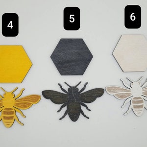 Puede incluir: Tres formas hexagonales de madera en amarillo, negro y blanco, con tres recortes de abejas de madera en marr&oacute;n, negro y blanco. Los hex&aacute;gonos est&aacute;n numerados 4, 5 y 6.