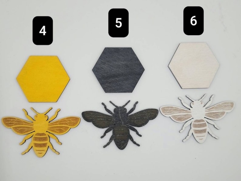 Puede incluir: Tres formas hexagonales de madera en amarillo, negro y blanco, con tres recortes de abejas de madera en marr&oacute;n, negro y blanco. Los hex&aacute;gonos est&aacute;n numerados 4, 5 y 6.