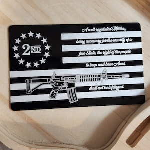 May include: A black and silver metal card with a stylized image of a rifle and the text "A well regulated Militia, being necessary for the security of a free State, the right of the people to keep and bear Arms, shall not be infringed." The card also features a circle of stars with the text "2ND" in the center.