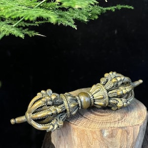 Peut inclure: Un objet rituel vajra en métal de couleur bronze présentant des sculptures symétriques complexes de griffes incurvées et une poignée centrale sphérique. L'article affiche une finition antique patinée avec des détails en relief sur toute sa structure.