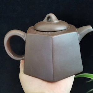 Puede incluir: Tetera marrón geométrica con tapa a juego. La tetera tiene un asa curva y un pico. La tetera está hecha de un material mate y tiene un diseño simple y elegante. Aproximadamente 15 cm de ancho y 10 cm de alto.