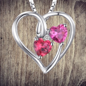 May include: A silver heart-shaped pendant necklace with two pink heart-shaped gemstones and a smaller clear gemstone.