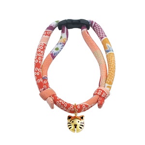 May include: A red, orange, and purple patterned cat harness with a gold cat-shaped bell charm.